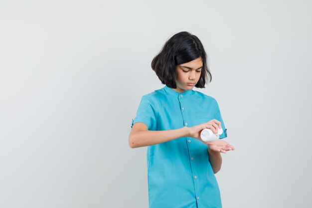 Junge Dame, die einige Pillen von der Flasche im blauen Hemd nimmt