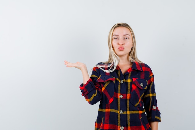 Junge Dame, die etwas hält, während Lippen im karierten Hemd schmollt und niedliche Vorderansicht schaut.