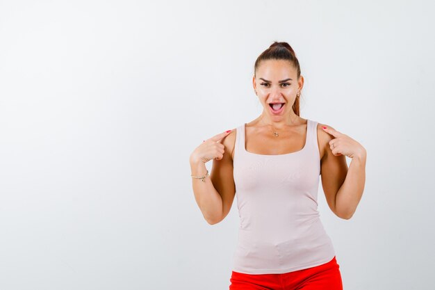 Junge Dame, die Finger auf Schultern im beigen Trägershirt hält und lustig aussieht