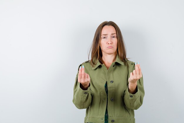 Junge Dame, die Geldgeste in Bluse, Jacke und wehmütigem Blick zeigt, Vorderansicht.