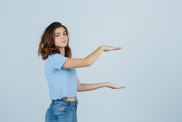 Junge Dame, die großes Zeichen zeigt, während Kamera in T-Shirt, Jeans und glückliche Vorderansicht betrachtend betrachtet.