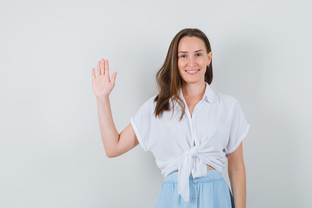 Junge Dame, die Grußgeste in Bluse und Rock zeigt und froh aussieht