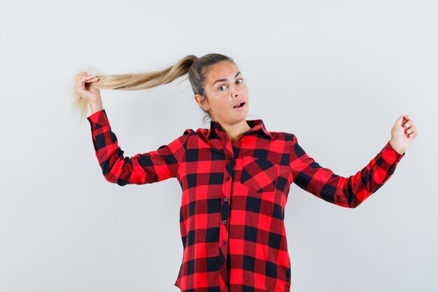 Junge Dame, die Haarsträhne im karierten Hemd hält und elegant aussieht