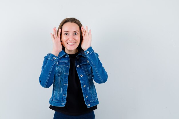 Junge Dame, die Händchen hält, um in Bluse, Jacke und neugierig zu sehen, Vorderansicht.