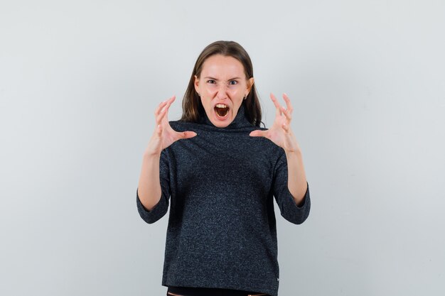 Junge Dame, die Hände auf aggressive Weise in der Vorderansicht des Freizeithemdes anhebt.