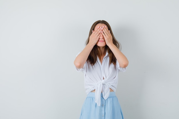 Junge Dame, die Hände auf Augen in Bluse, Rock hält und aufgeregt schaut