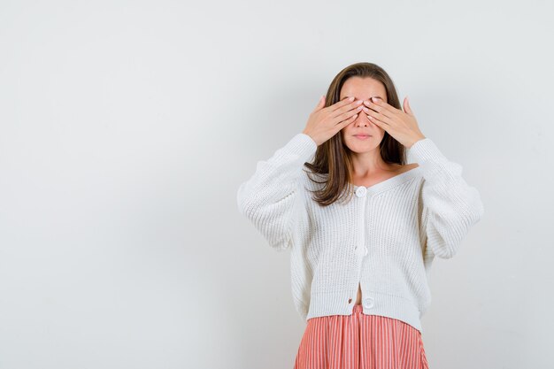 Junge Dame, die Hände auf Augen in Strickjacke und Rock hält, die niedlich lokalisiert suchen