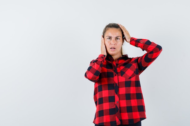 Junge Dame, die Hände auf Kopf im karierten Hemd hält und ratlos aussieht