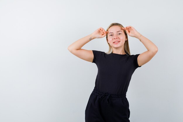 Junge Dame, die Hände auf Kopf in T-Shirt, Hose und freudig aussehend hält. Vorderansicht.