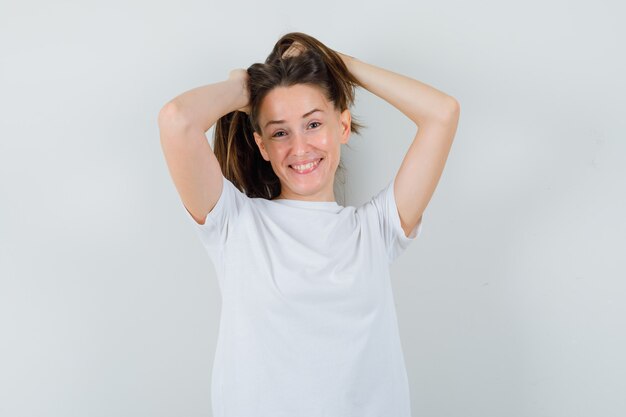 Junge Dame, die Hände im Haar im weißen T-Shirt hält und faszinierend schaut