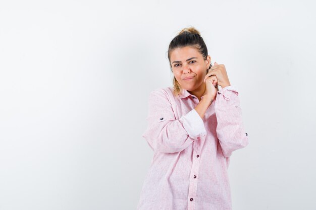 Junge Dame, die Hände im rosa Hemd gefaltet hält und charmant aussieht