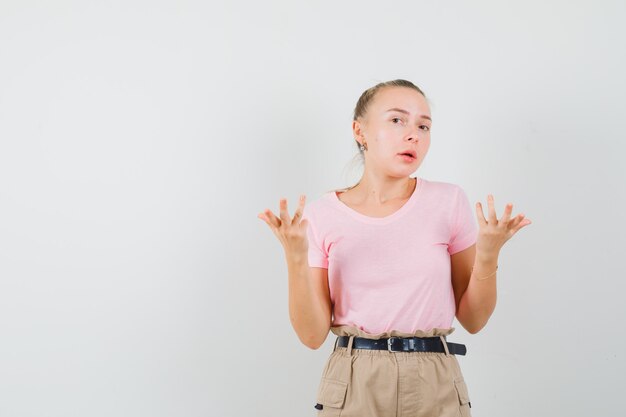 Junge Dame, die Hände in fragender Geste in T-Shirt und in Hosen hebt und verwirrt aussieht