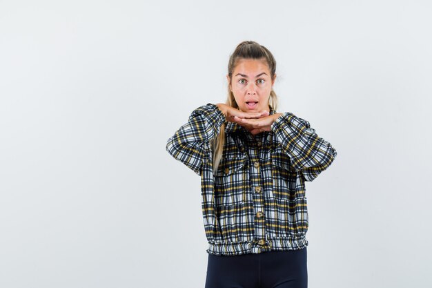 Junge Dame, die Hände unter Kinn im Hemd, in den Shorts hält und erstaunt, Vorderansicht schaut.