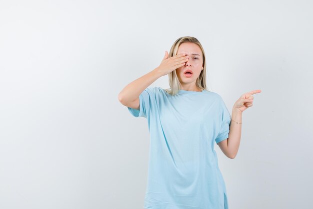 Junge Dame, die Hand am Auge hält, während sie auf die rechte Seite im T-Shirt zeigt, isoliert