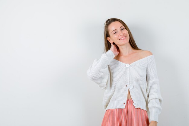 Junge Dame, die Hand am Hals in Strickjacke und Rock hält, die glücklich lokalisiert suchen