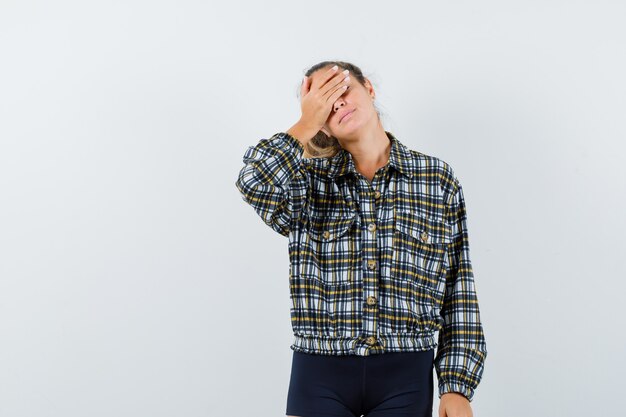 Junge Dame, die Hand auf Augen im Hemd, in den Shorts hält und fesselnd, Vorderansicht schaut.