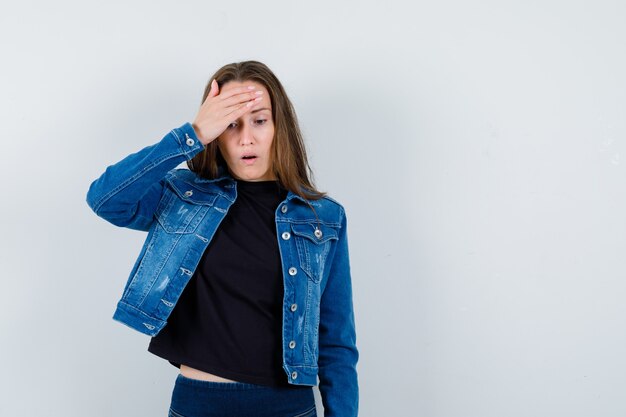 Junge Dame, die Hand auf dem Kopf in Bluse, Jacke hält und vergesslich aussieht, Vorderansicht.