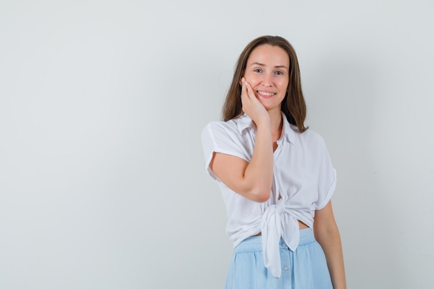 Junge Dame, die Hand auf ihren Wangen hält, während sie in Bluse und Rock lächelt und froh aussieht