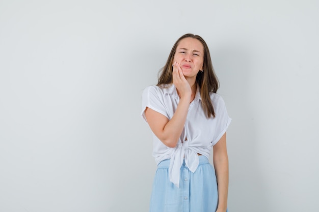 Junge Dame, die Hand auf ihrer Wange in Bluse, Rock hält und schmerzhaft aussieht