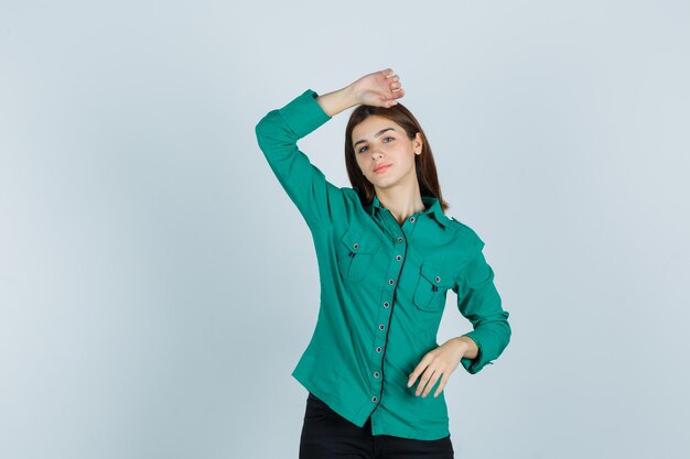 Junge Dame, die Hand auf Kopf im grünen Hemd hält und nachdenklich, Vorderansicht schaut.