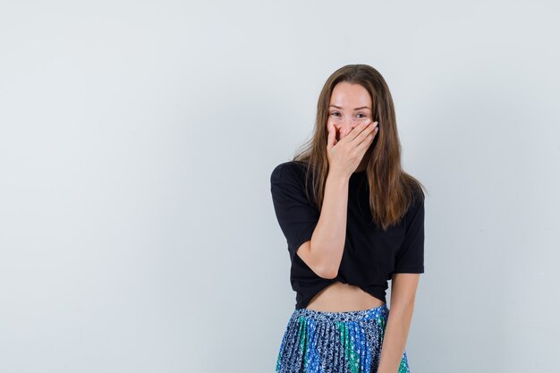 Junge Dame, die Hand auf Mund in Bluse, Rock hält und glücklich schaut