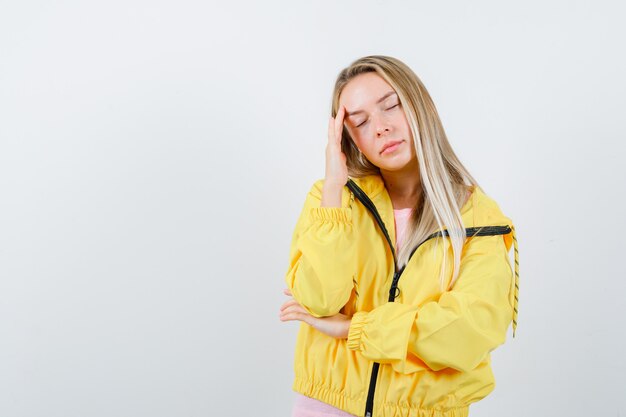 Junge Dame, die Hand auf Schläfe im T-Shirt, in der Jacke hält und erschöpft schaut