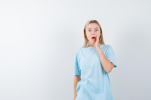 Junge Dame, die Hand auf Wange im T-Shirt hält und verwirrt schaut