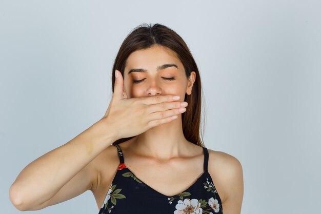 Junge Dame, die Hand in Bluse am Mund hält und friedlich aussieht. Vorderansicht.