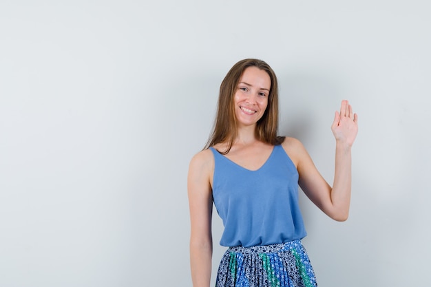 Junge Dame, die Hand winkt, um sich im Unterhemd, im Rock zu verabschieden und fröhlich, Vorderansicht zu schauen.