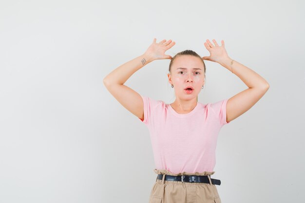 Junge Dame, die Handflächen in Übergabegeste in T-Shirt und in Hosen hebt und ängstlich aussieht