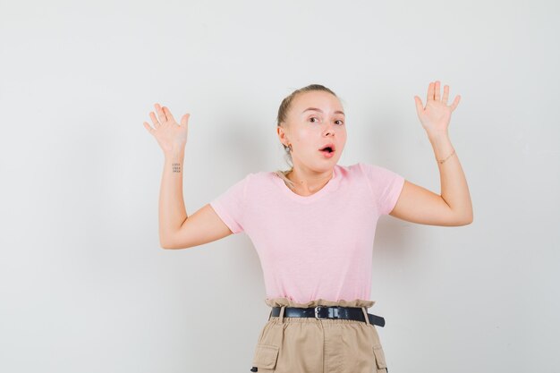 Junge Dame, die Handflächen in Übergabegeste in T-Shirt und in Hosen zeigt und ängstlich aussieht