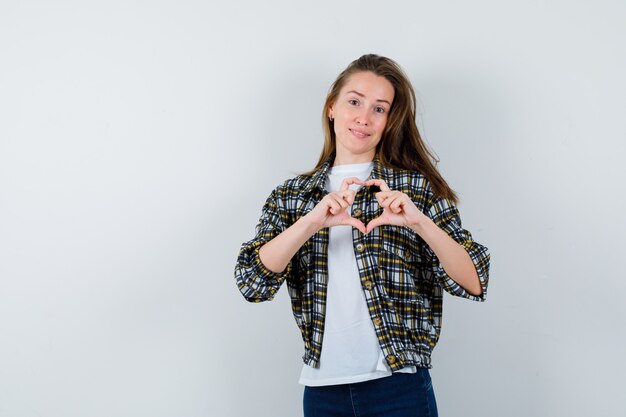 Junge Dame, die Herzgeste in T-Shirt, Jacke, Jeans zeigt und niedliche Vorderansicht schaut.