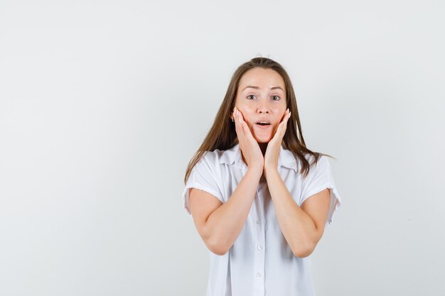 Junge Dame, die ihr Gesicht mit den Händen in der weißen Bluse hält und besorgt aussieht.