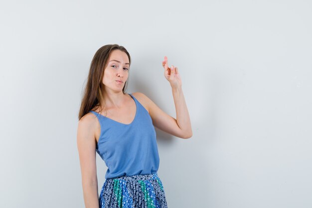 Junge Dame, die ihre gekreuzten Finger in der blauen Bluse, im Rock und in der selbstbewussten Vorderansicht zeigt.