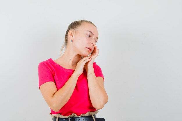 Junge Dame, die ihre Gesichtshaut auf Wange im rosa T-Shirt berührt und niedlich aussieht