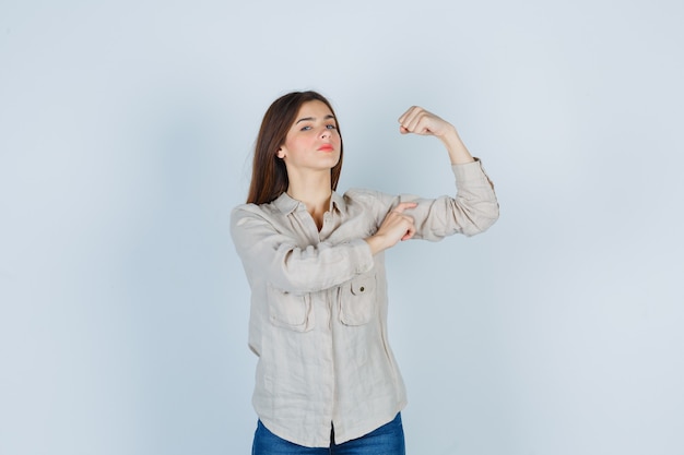 Junge Dame, die ihre Muskeln in lässigen Jeans zeigt und selbstbewusst aussieht, Vorderansicht.