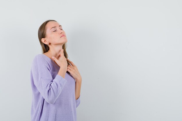 Junge Dame, die ihren Hals im Freizeithemd berührt und friedlich aussieht