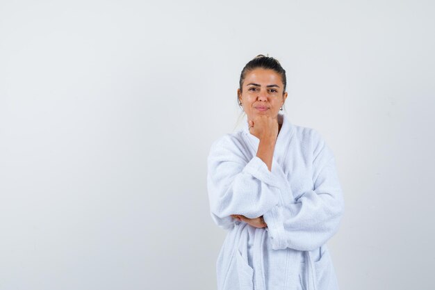 Junge Dame, die im Bademantel das Kinn auf die Faust stützt und selbstbewusst aussieht