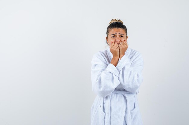 Junge Dame, die im Bademantel den Mund mit Fäusten bedeckt und verwirrt aussieht