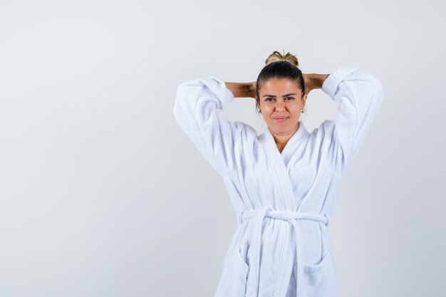 Junge Dame, die im Bademantel die Hände hinter dem Kopf hält und selbstbewusst aussieht looking