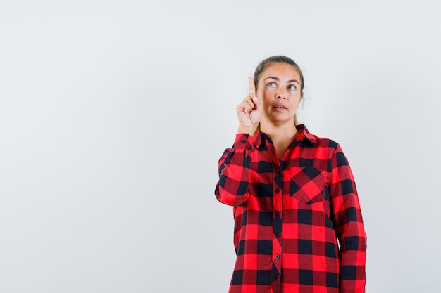 Junge Dame, die im karierten Hemd nach oben zeigt und nachdenklich aussieht