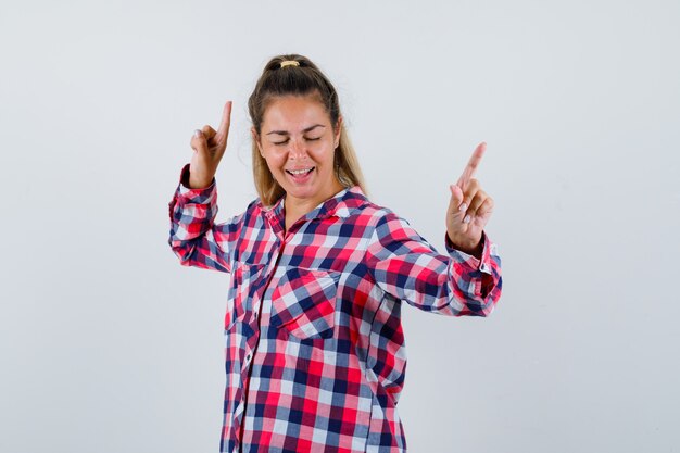 Junge Dame, die im karierten Hemd nach oben zeigt und verspielte Vorderansicht sieht.