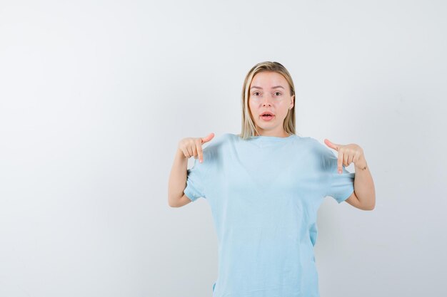 Junge Dame, die im T-Shirt nach unten zeigt und verwirrt isoliert aussieht