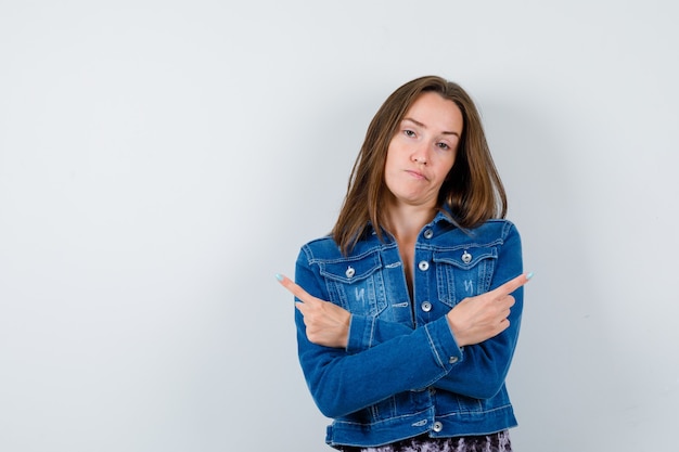 Junge Dame, die in Bluse, Jeansjacke auf beide Seiten zeigt und unentschlossen aussieht. Vorderansicht.