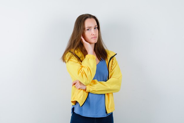 Junge Dame, die in denkender Haltung in T-Shirt, Jacke steht und vernünftig aussieht. Vorderansicht.