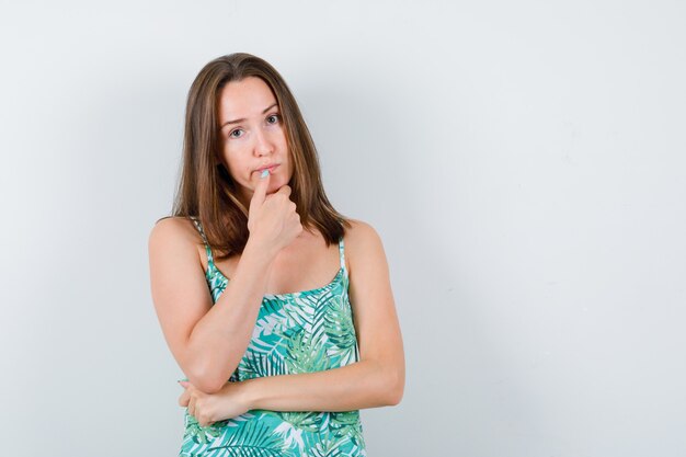 Junge Dame, die in denkender Pose in Bluse steht und nachdenklich schaut, Vorderansicht.