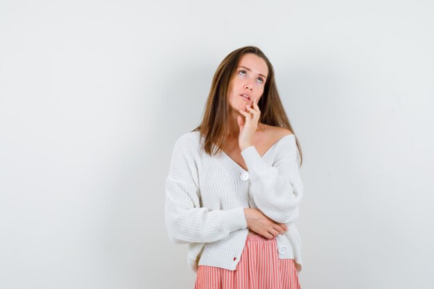 Junge Dame, die in denkender Pose in Strickjacke und Rock steht und zögernd isoliert schaut