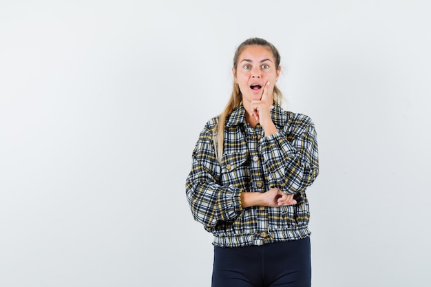 Junge Dame, die in der denkenden Pose im Hemd, in den kurzen Hosen und in der überraschten Vorderansicht steht.