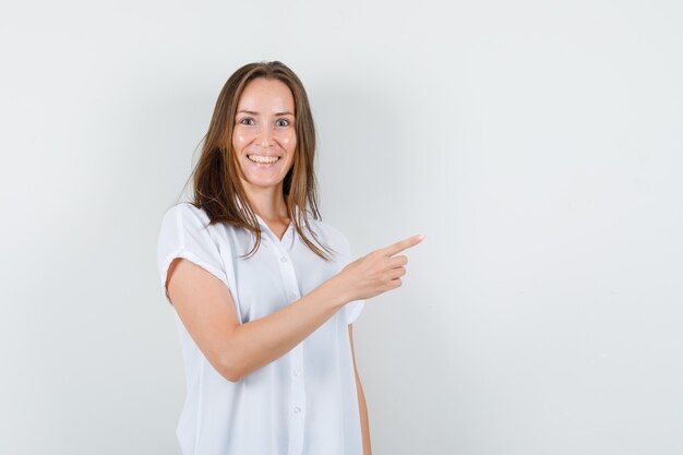 Junge Dame, die in der weißen Bluse beiseite zeigt und erfreut aussieht.