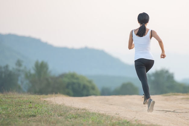 Junge Dame, die in einem gesunden Lebensstil genießt, während sie entlang einer Landstraße, Übung und Fitness und Training im Freien joggt.